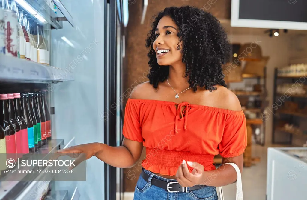 Happy, grocery shopping and woman in a supermarket with drinks at a retail store in Sao Paulo. Happiness, smile and girl from Brazil buying a beverage on a shelf in a food shop while on vacation.