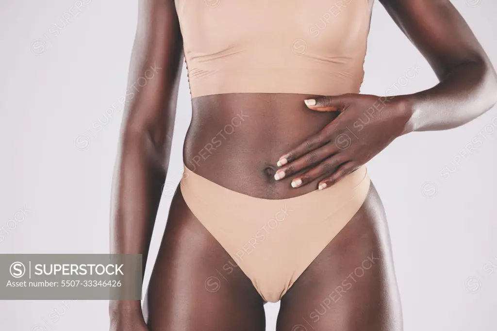 Hand, stomach and body with a model black woman touching her tummy in studio on a gray background for wellness. Health, underwear and diet with a female posing for healthy eating or lifestyle