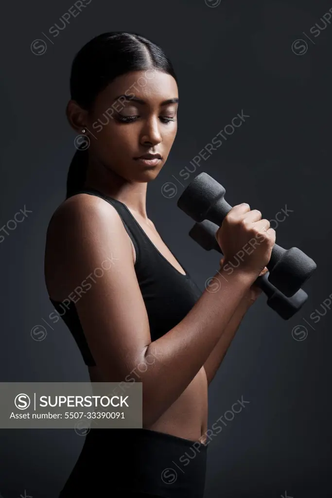 Sports, serious and woman with dumbbell for workout in studio isolated on a black background. Strong, bodybuilder and Indian female athlete weightlifting for muscle, training and fitness exercise.