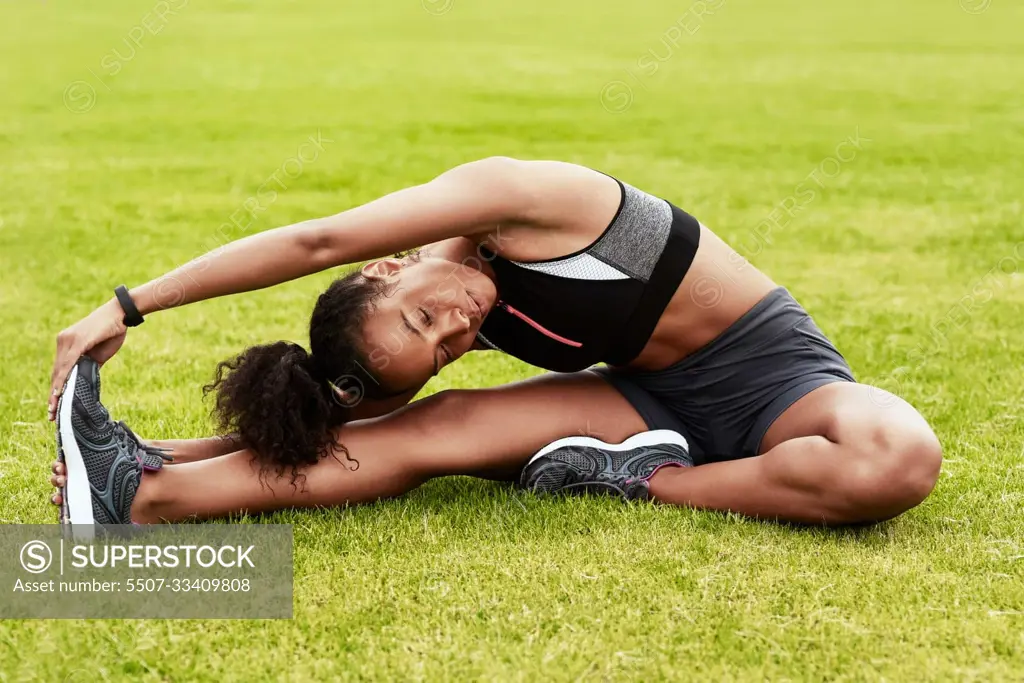 Youve gotta be flexible. Full length shot of an attractive young female athlete warming up at the track.