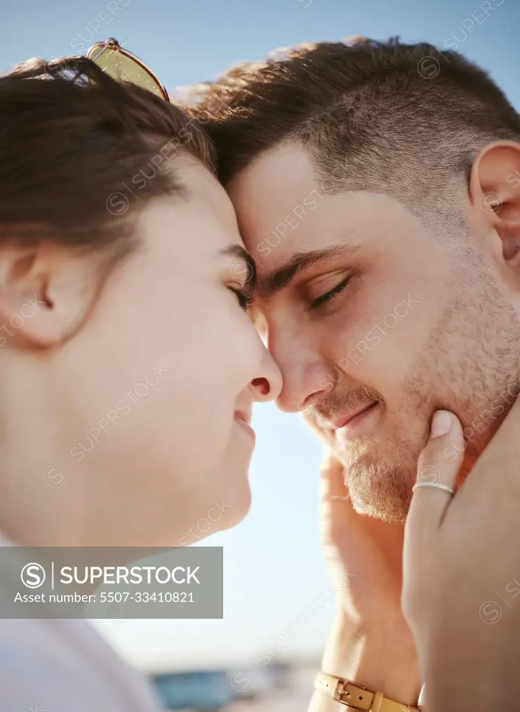 Love, touching face and couple on the beach, woman holding man with heads together. Summer, romance and loving happy couple on holiday. Real people, vacation and people in love bonding and affection