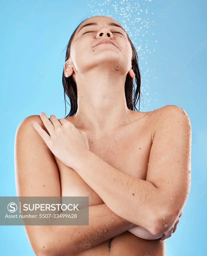 Shower, body and woman in the nude with water for cleaning, grooming and  hygiene against a blue studio background. Skin, wellness and happy Asian  model with peace, calm and relax while showering -