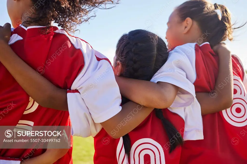 Girl, soccer group and back with huddle on field for match, contest or game with team building support. Female kids, football player children and hug for solidarity, diversity or motivation on pitch