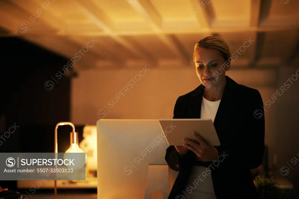 Working above and beyond office hours. a mature woman using her digital tablet while working late at the office.