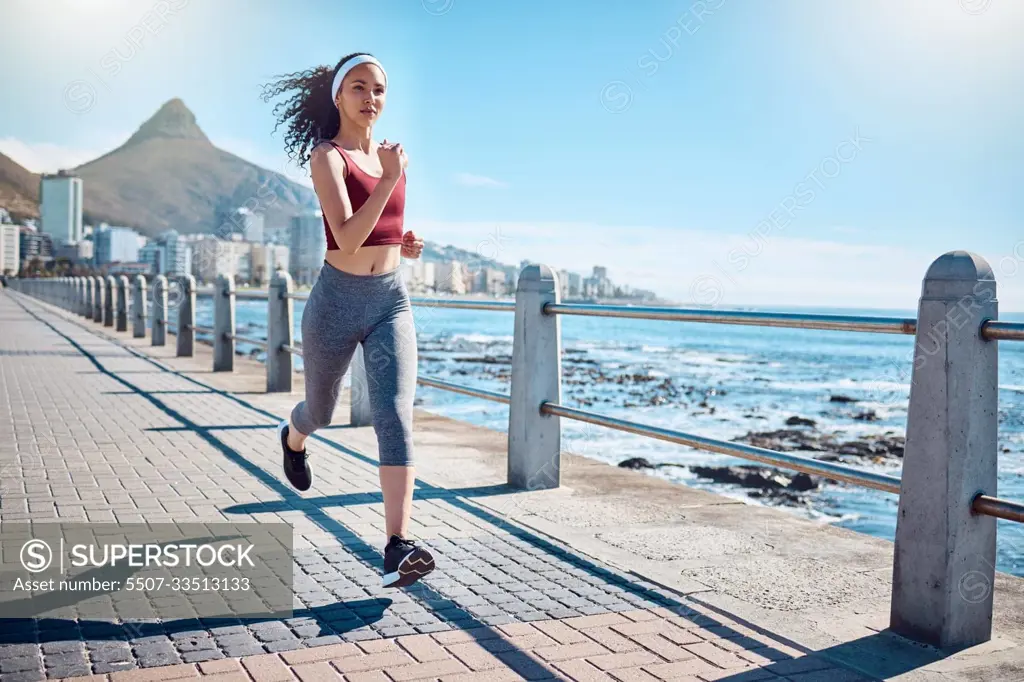 Woman running at ocean promenade for fitness, energy and strong body in Cape Town. Female runner, sports person and athlete at seaside for marathon, cardio exercise and healthy summer workout in sun