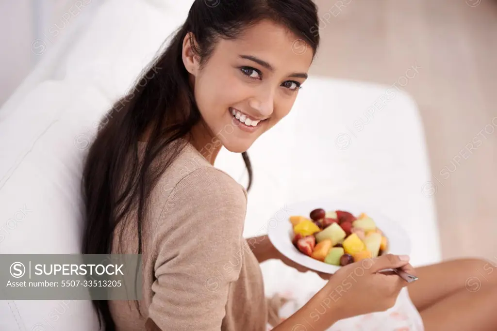 Fresh fruit for a healthy lifestyle. A beautiful young woman enjoying a healthy snack from the comfort of her couch.