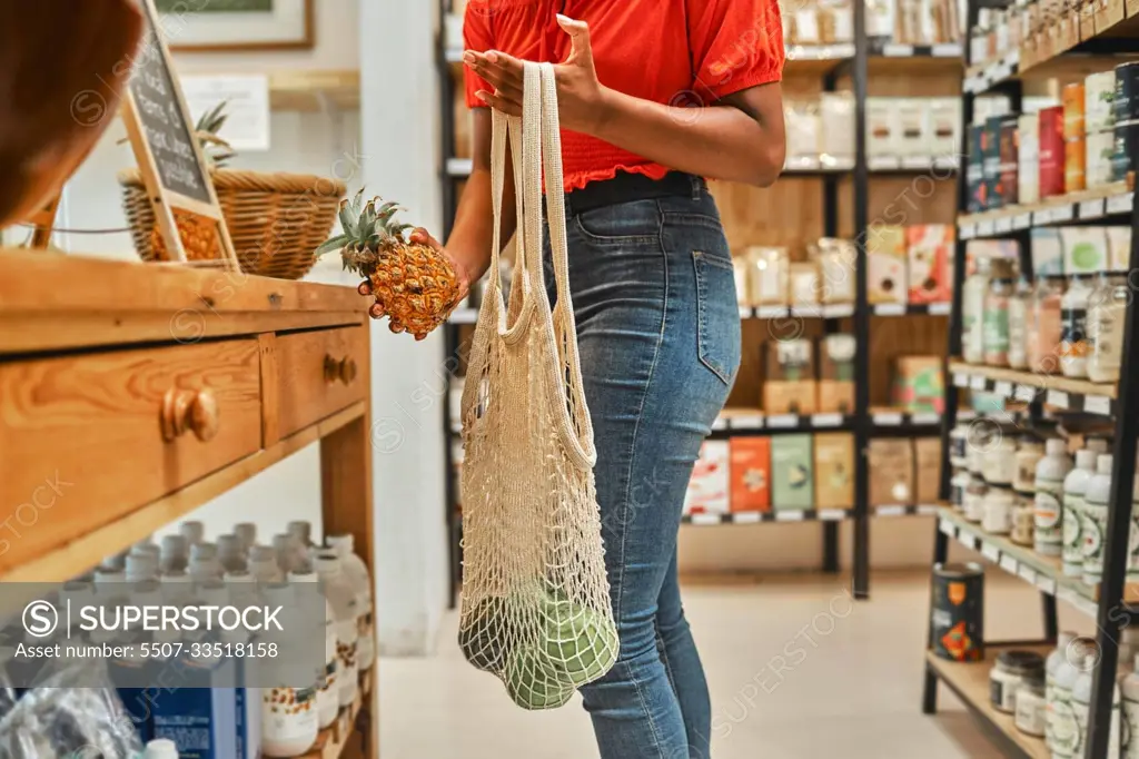 Woman, fruit shopping and pineapple in hand with ripe avo in bag at a supermarket grocery store looking for healthy food at discount price. Healthy, organic and natural fresh groceries for home lunch