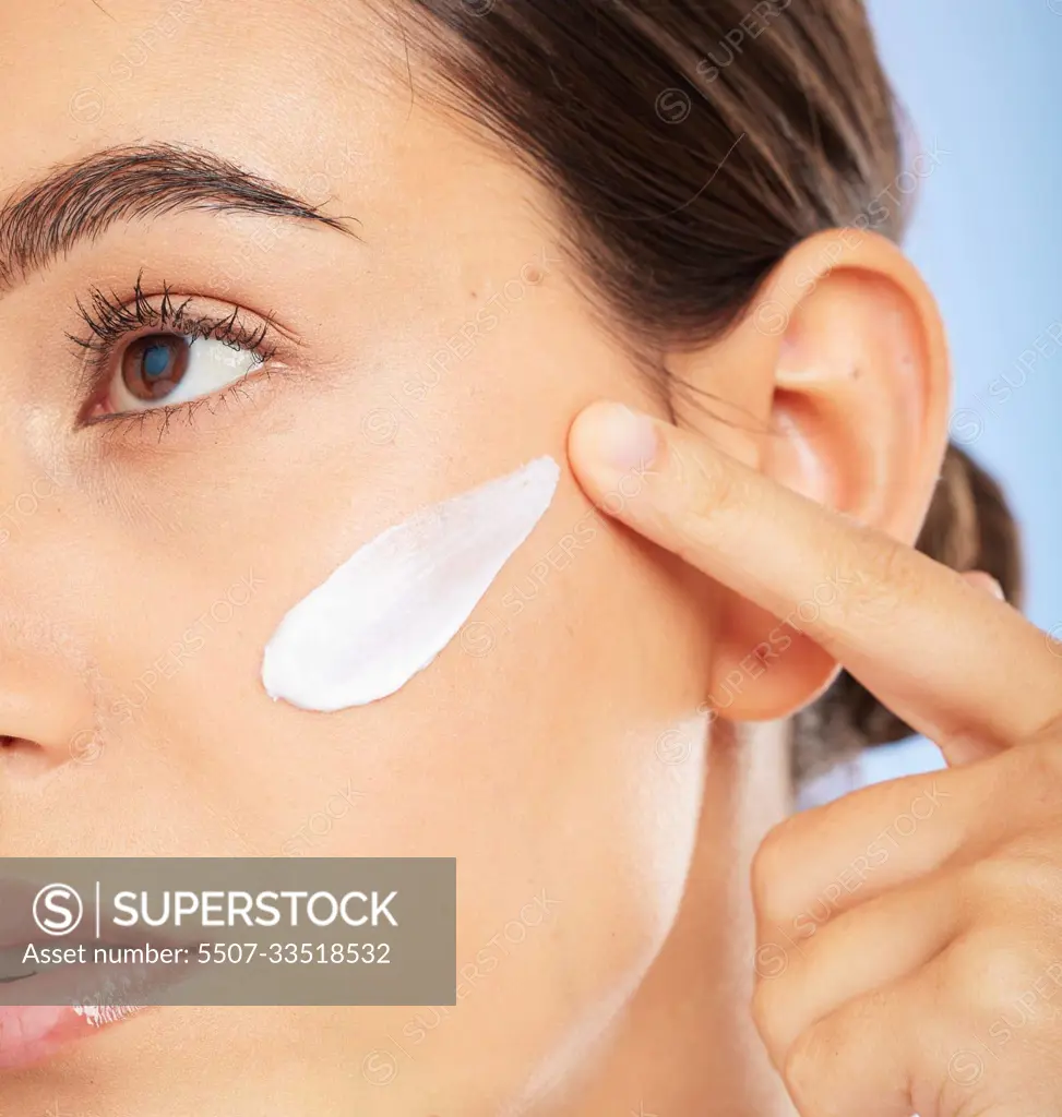 Face, beauty skincare and woman with cream in studio isolated on a blue background. Thinking, cosmetics and female model apply facial lotion, creme and moisturizer product for healthy skin hydration.