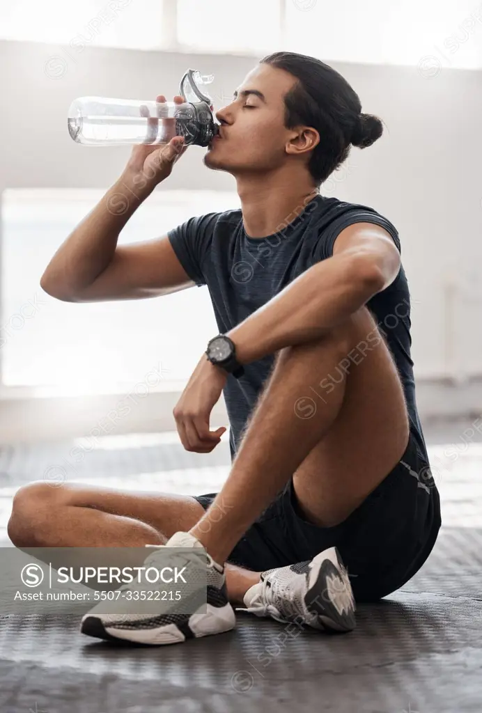 Water bottle, fitness and gym man tired after a fitness training, exercise challenge and wellness goal with healthy diet or nutrition. Young sports person floor drinking water for healthy lifestyle