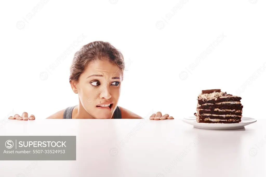 Hungry, temptation and a woman with chocolate cake on a table isolated on a white background in a studio. Unhealthy, sneaky and a young lady looking at a dessert while on a diet or healthy lifestyle