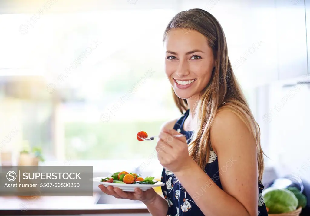 Eat healthy to live healthy. Portrait of a young woman eating a bowl of strawberries at home.