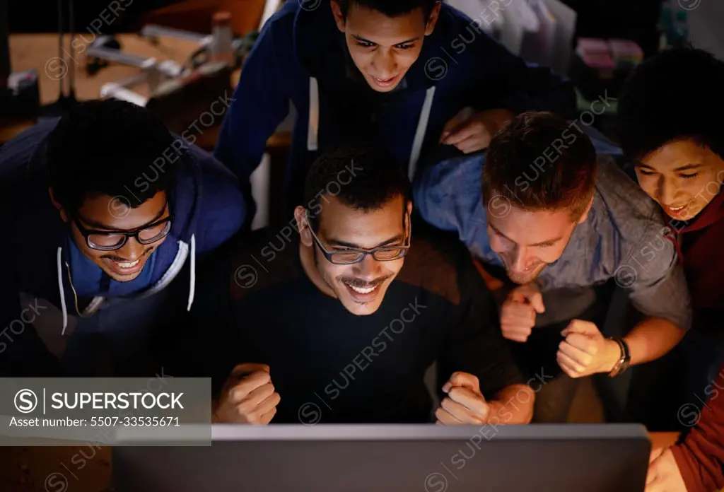 Getting behind the team. a group of young man cheering at a monitor in a dark room.