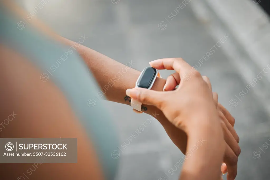 Cropped view of a fit female athlete checking the time and pulse on her watch to track her progress while taking a break from working out in the city