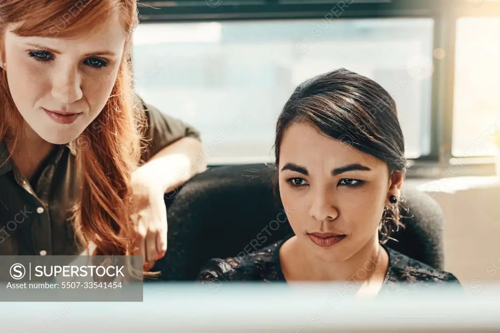 Teamwork makes the task work. two young businesswomen using a computer together in a modern office.