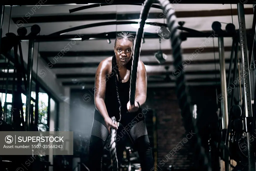 Ready for battle. Cropped portrait of an attractive young female athlete working out with battle ropes in the gym.