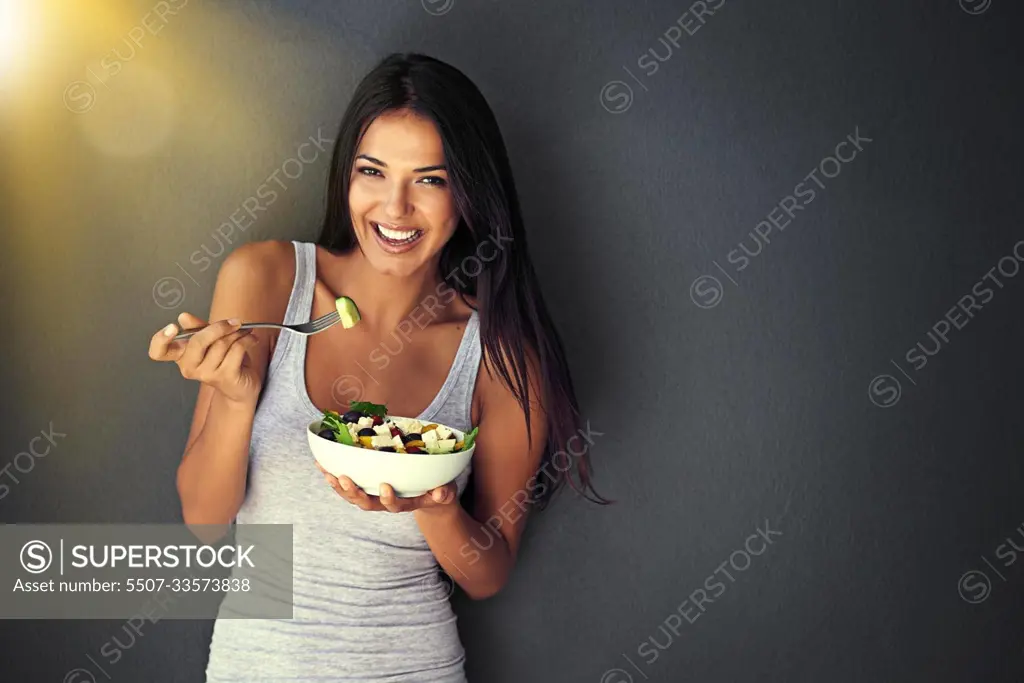 Healthy and delicious. Portrait of a healthy young woman eating a salad against a gray background.