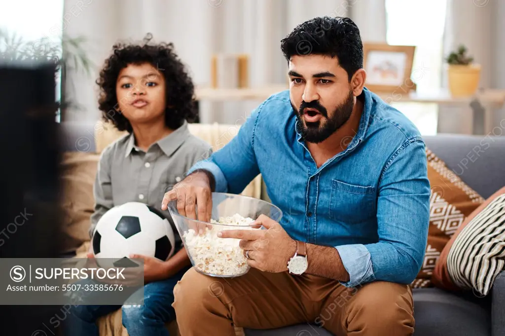 Were both avid sports fans. Cropped shot of an adorable little boy watching a football game with his father on tv at home.