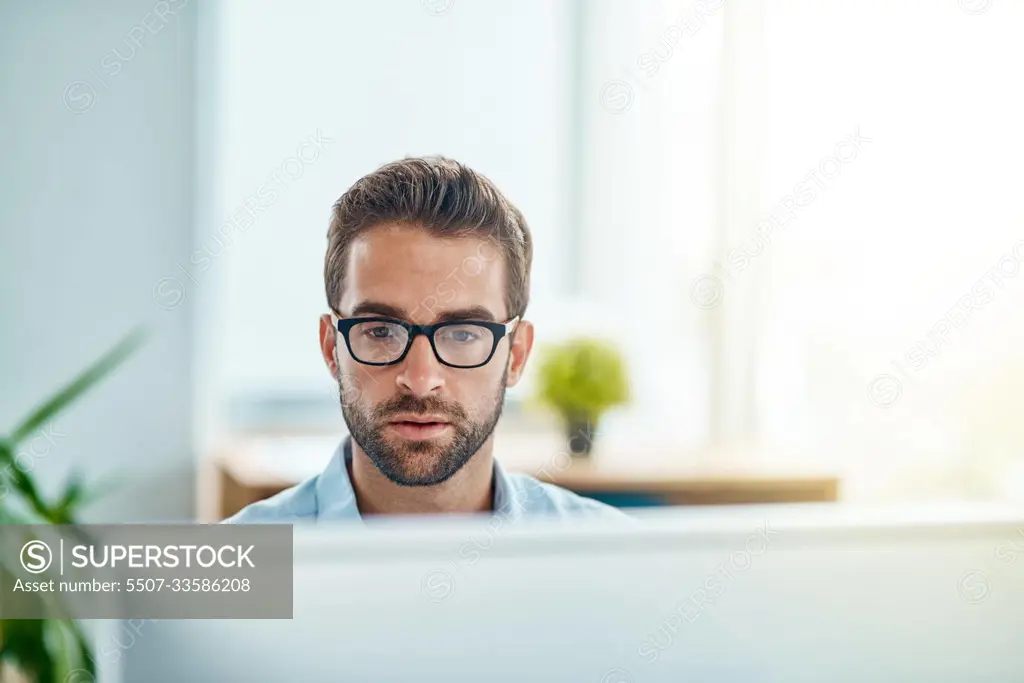 Busy at work as usual. Shot of a young businessman working on a computer in an office.