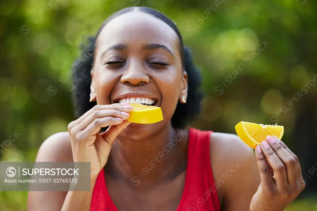 Black woman, vitamin C and eating orange slice for natural nutrition or citrus diet in nature outdoors. Happy African female person enjoying bite of organic fruit for health and wellness in the park