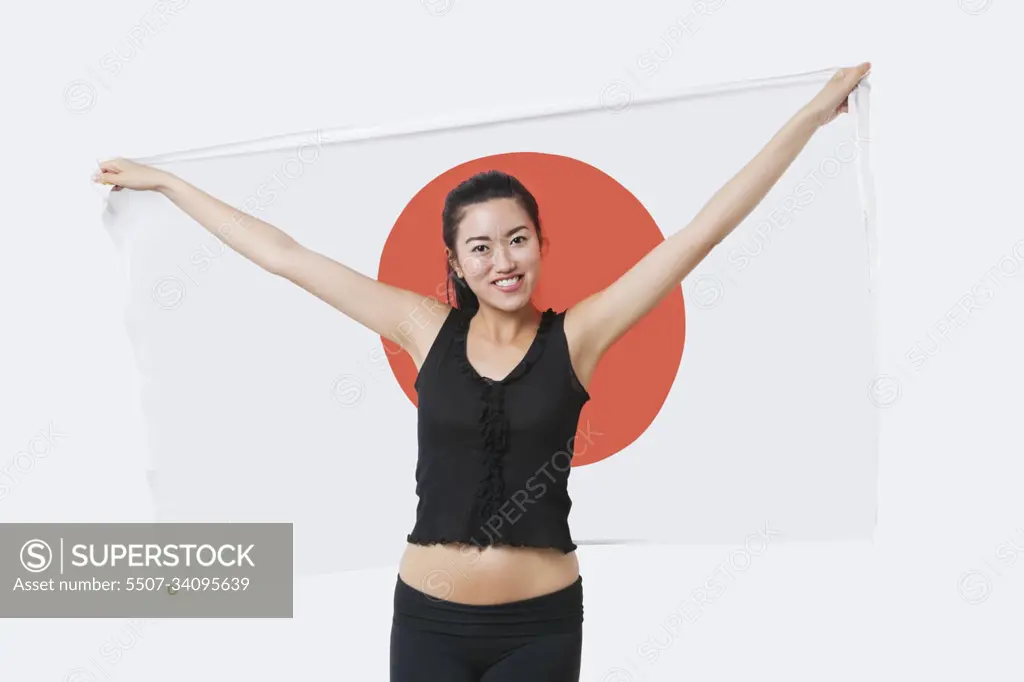 Portrait of smiling young woman holding Japanese flag over white background