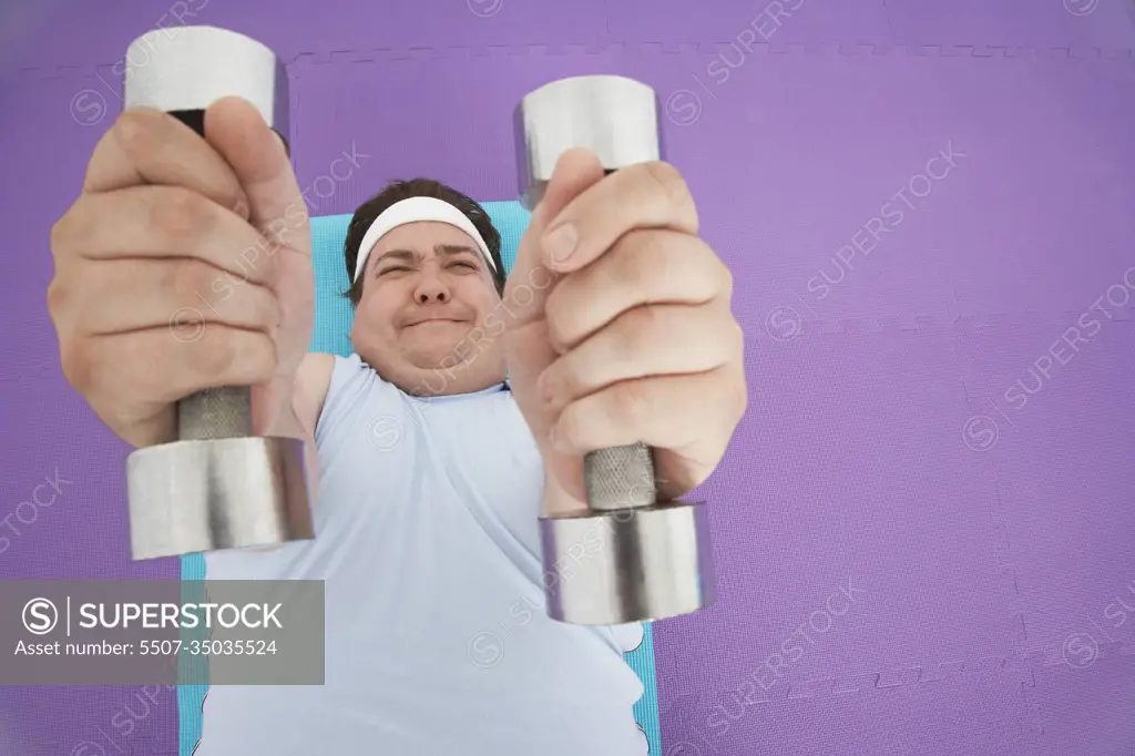 Overhead view of an overweight man lying down and lifting dumbbells