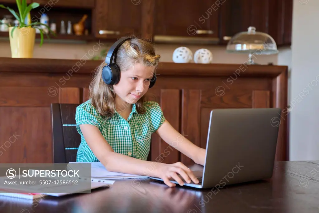 Pre-teen girl with laptop and headphones studies at home.