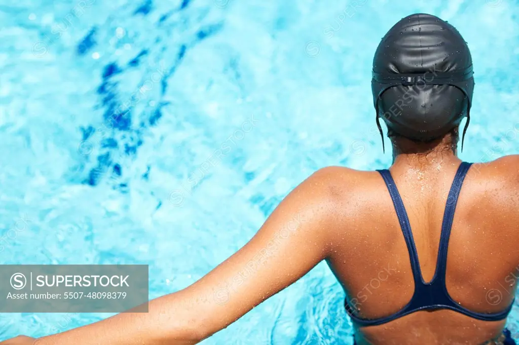 Back, swimming and pool with a sports woman for training, cardio workout or exercise for fitness. Female athlete person or professional swimmer in clear blue water for competition in swimsuit