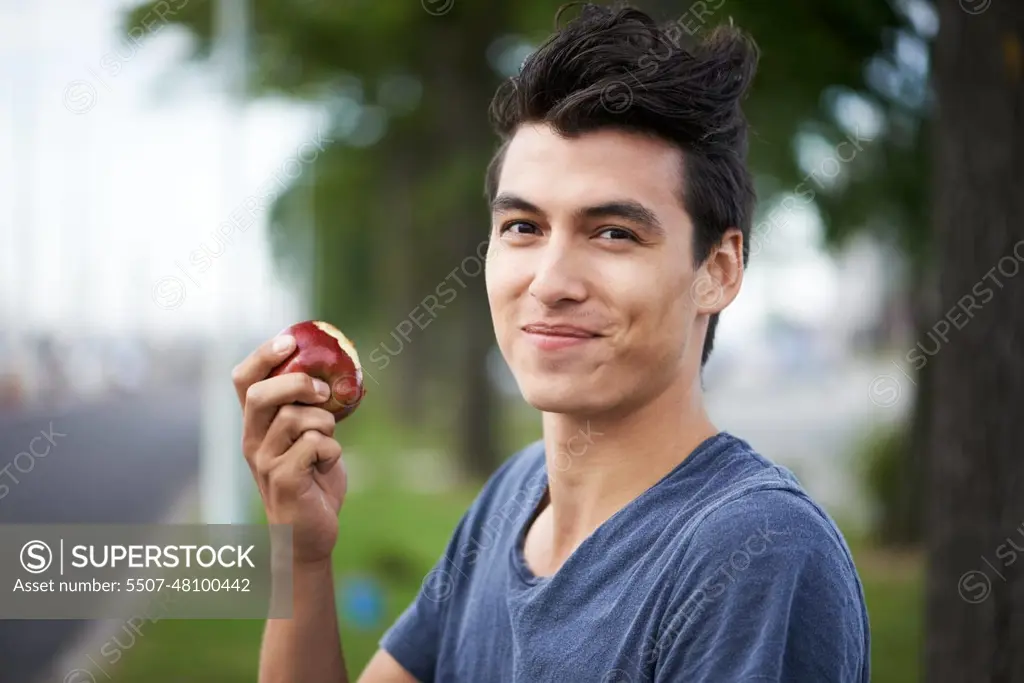 Man, smile and eating an apple, health and wellness in portrait, nutrition and vitamins for vegan. Happy male person, fruit and organic or natural, breakfast and diet in outdoors, fresh and digestion