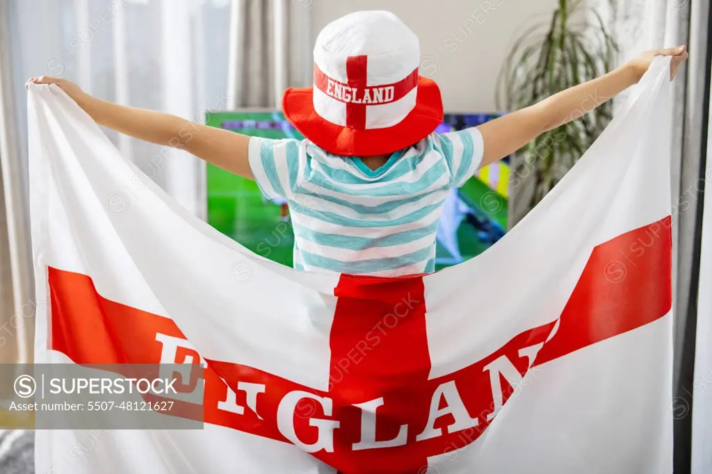 A boy holding England flag and watching soccer game on TV at home