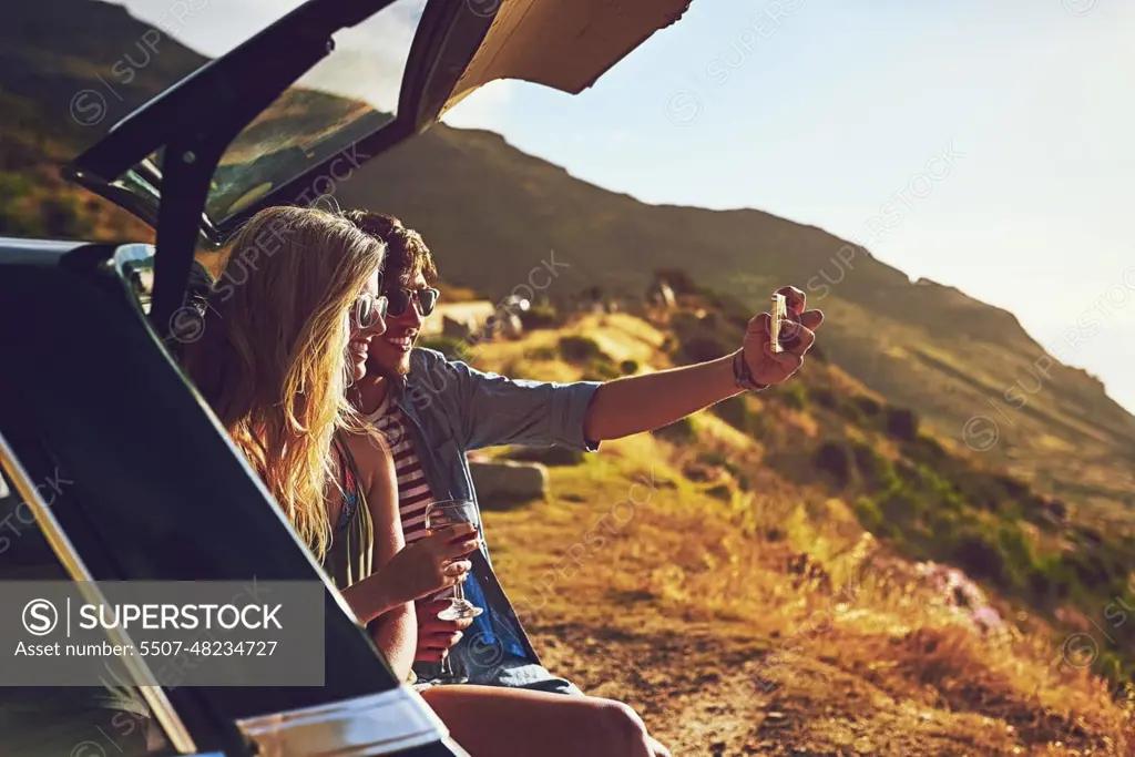 Roadtripping. a happy young couple posing for a selfie with their car on a roadtrip.