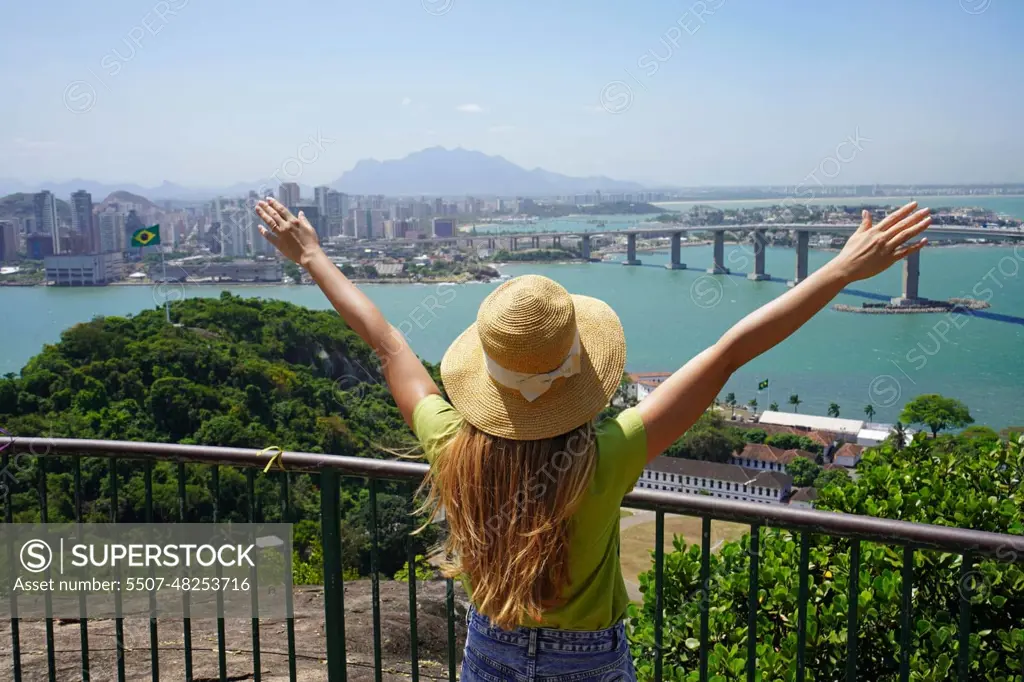 Joyful girl visiting Brazil. Beautiful young woman with raised arms enjoying view of Vitoria cityscape the capital of Espirito Santo state in Brazil.