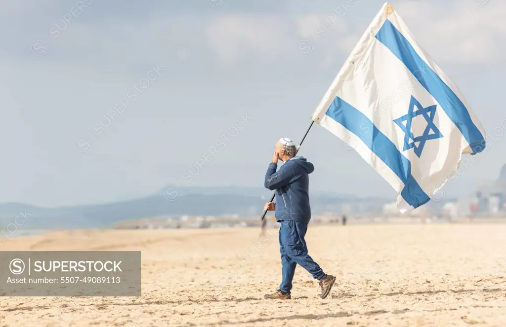 25 november 2023, Lisbon, Portugal - A Man Walking on a Beach Holding a Flag of Israel