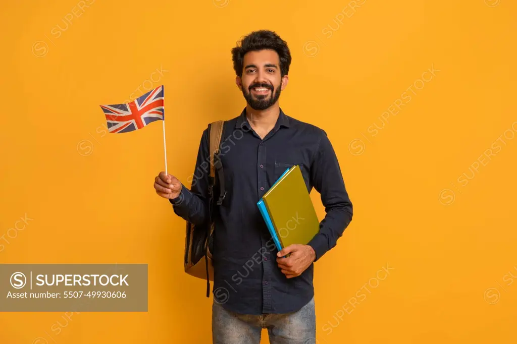 Language Courses. Smiling Young Indian Man Holding British Flag And Workbooks