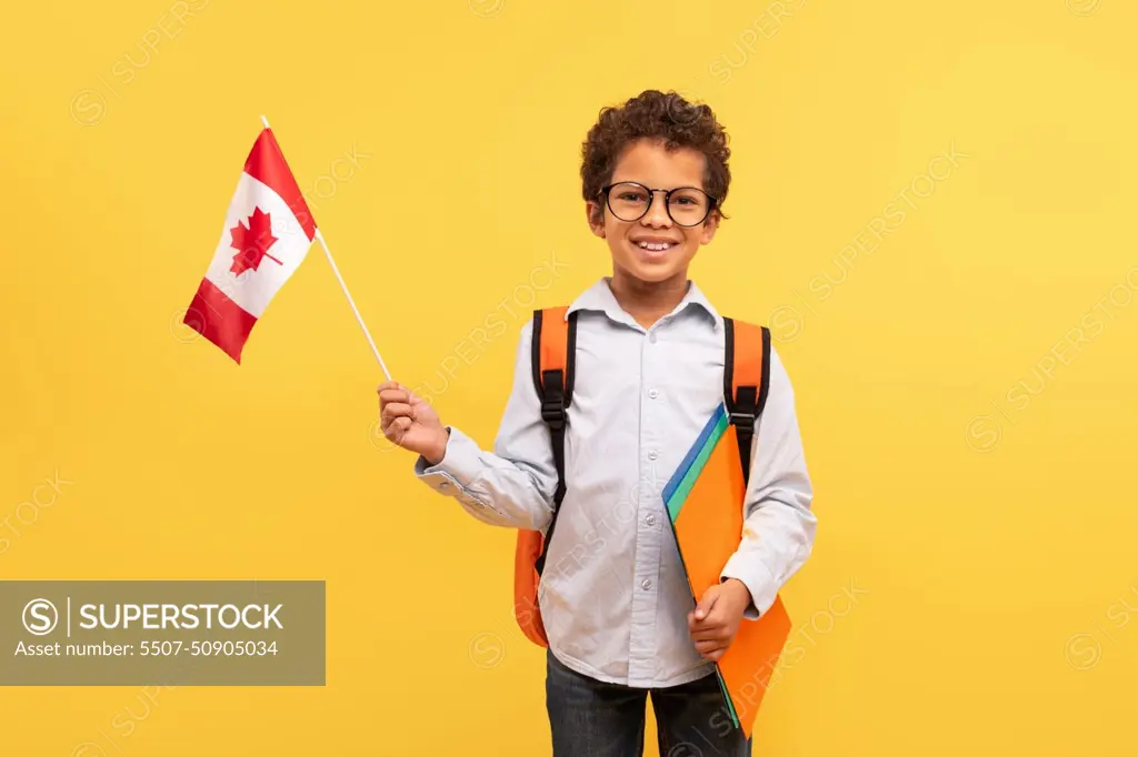 Proud schoolboy holding Canadian flag on yellow background