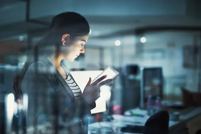 Alone in the office getting work done. Shot of a young businesswoman working late in the office.