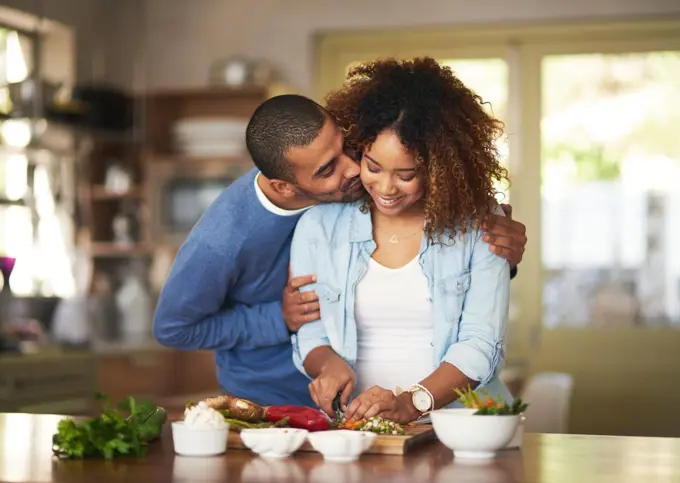 The healthy marriage is a happy marriage. Shot of a young man kissing his wife while she prepares a healthy meal at home.