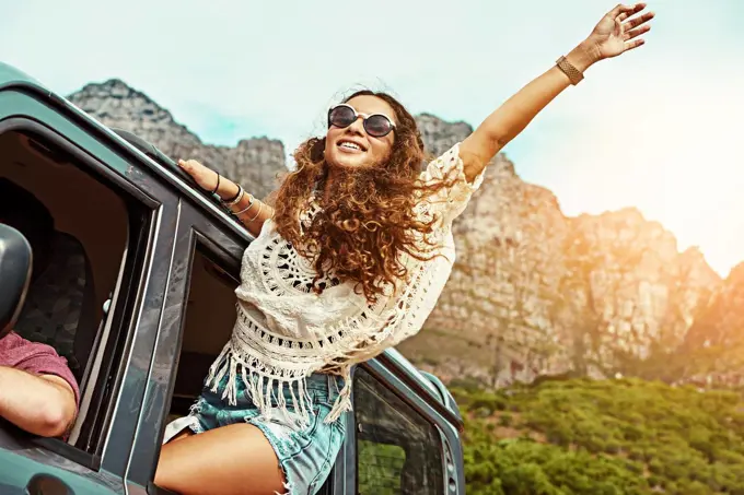 Bring on the good times. Cropped shot of a young woman leaning out a car with her arms outstretched while on a roadtrip.