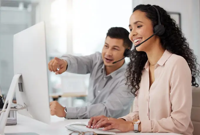 Sharing advice on how to better their services. Shot of two call centre agents working together on a computer in an office.