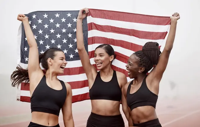 We finally did it. Shot of female athletes celebrating their win while holding a flag.