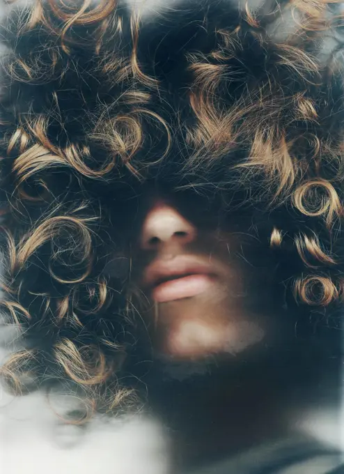 Hiding within himself. Young man with his face obscured by his long, curly hair.