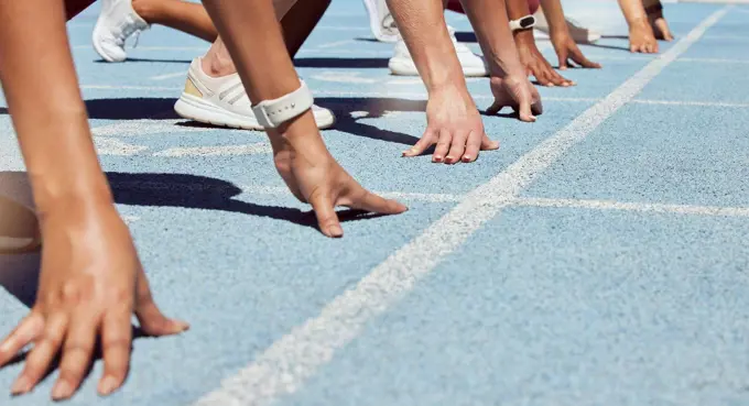 Closeup of determined group of athletes in starting position line to begin sprint or run race on sports track stadium. Hands of diverse sports people ready to compete in track and field olympic event