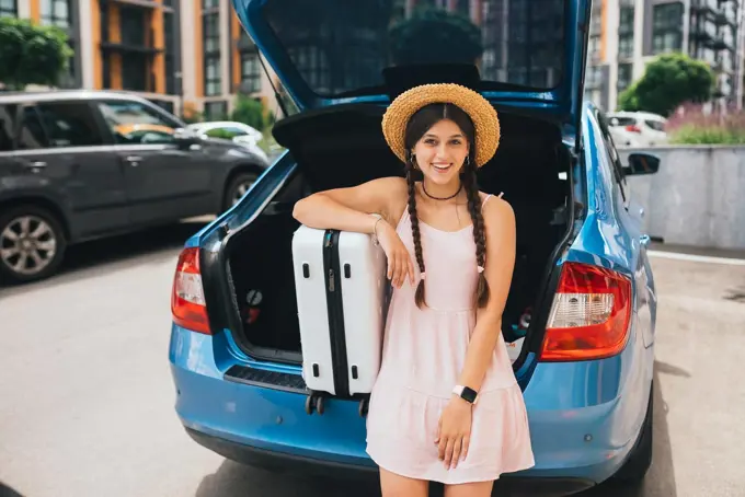 Woman packing her suitcase into luggage boot of the car.