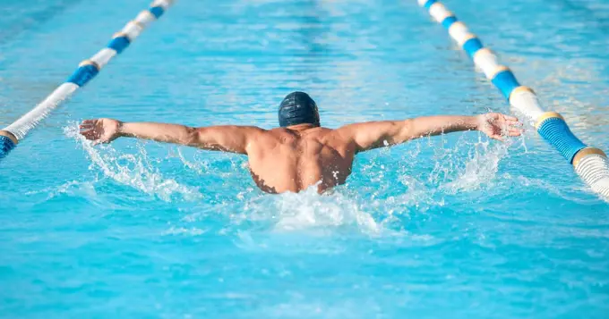 Thats some serious pace. an unrecognizable young male athlete swimming in an olympic-sized pool.