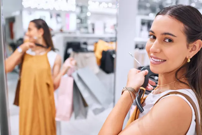 Portrait of a trendy young woman holding a dress against her deciding whether to buy it. Smiling female fitting on clothes in a store. Mixed race shopper happy about finding a sale and discount