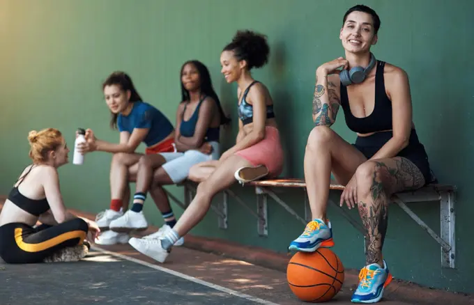 Chilling after another victory. Full length portrait of an attractive young female athlete sitting on a bench at the basketball court with her teammates in the background.