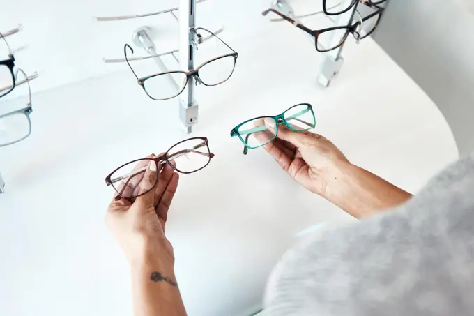 Buying, looking and shopping for glasses at a retail eyewear store and optometrist inside. Customer holding shop stock trying to decide on a new modern style, trendy and stylish frames to buy on sale