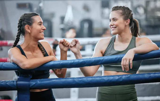 Giving support, motivation and bumping fists after being active, exercising and training in ring. Team of female boxers, fighters or sports athletes standing together in a gym, fitness center or club