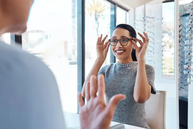 A customer buying, testing or trying on glasses at an optometrist store or shop. Health care eye wear professional picking or selling a pair of new eyeglasses to a young female client or patient.