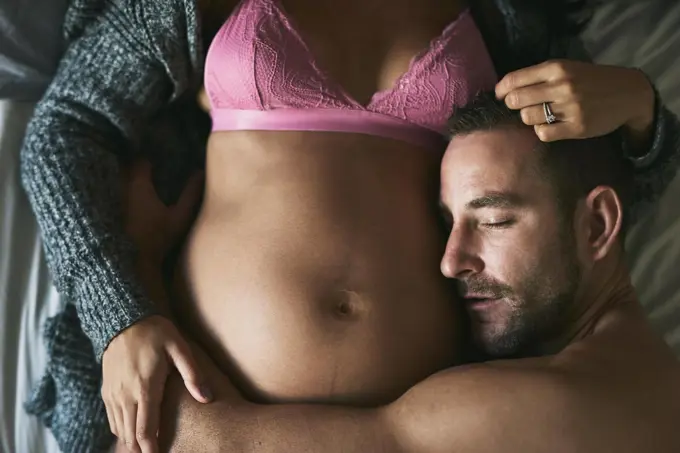 In love with his unborn child. High angle shot of a handsome young man loving his pregnant wife in their bedroom.