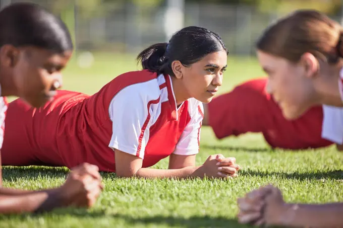 Women soccer players in a team doing the plank fitness exercise in training together on a practice sports field. Healthy female group of young athletes doing a core strength workout using teamwork